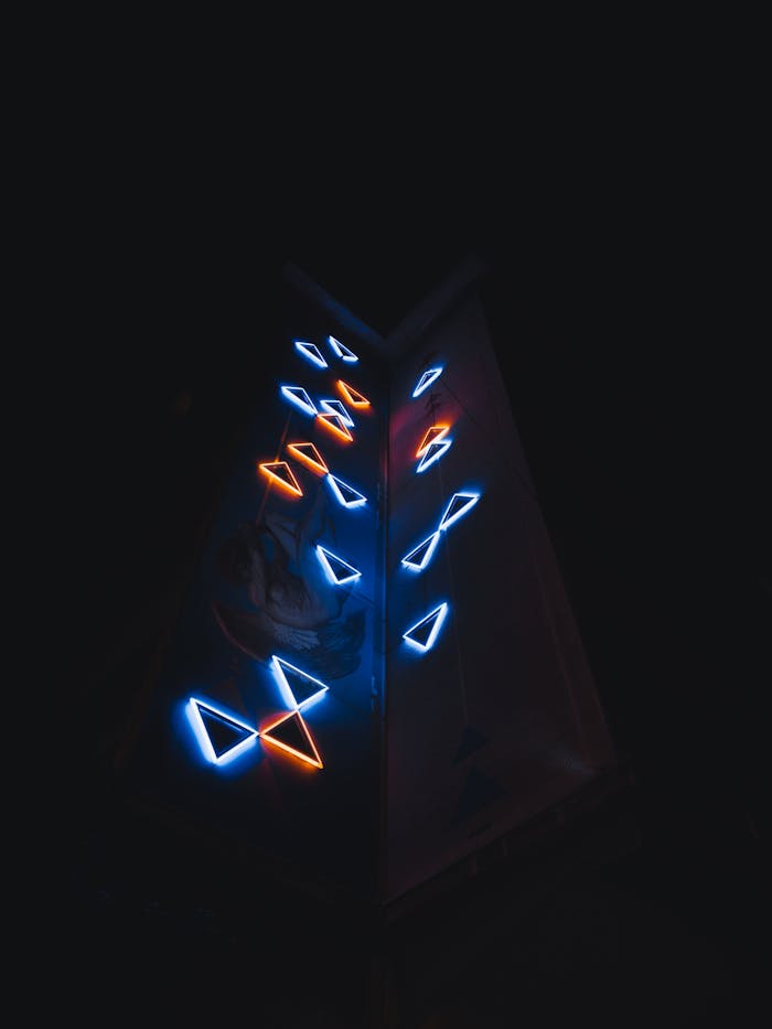 Triangular glass sculpture with glowing neon symbols against a dark background.